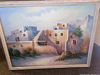 Front view of the large painting showing the entire artwork and frame, capturing the multi-leveled adobe-style building and ladders.