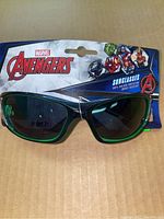 Front view of black and green framed Marvel Avengers sunglasses in packaging with visible branding and product details.