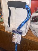Photo of new walking cane with blue swirl design and black foam grip. Wrist strap attached but frayed. Product tag visible with user image and specifications.