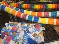 Photo showing three fabric-covered striped pool noodles and several packaged nose clip and ear plug sets on a surface.