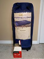 Photo of Cabela's Folding Airbed in wheeled blue storage bag with Sterno cookstove box in front.