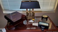 Photo shows two wooden memory boxes with brass clasps and a double-shade table lamp with brass base on a glass-top table.