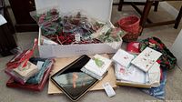 Full lot including Christmas plate, table linens, baskets, and faux flower decorations packed in a box and piled on floor.