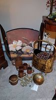 Copper pitcher, copper cups, brass fireplace screen with floral design, brass log bin with pine cones and fireplace tools laid out on carpet.