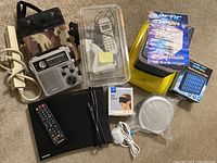 Full view of lot contents including Eton FR-300 radio, cordless phone, Arctic Air fan with filter, Sony Walkman CD player with earphones, black eye pillow, packing box, and remote controls.
