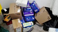 Corner view showing stacked purple TENA Intimates packages, green-labeled TENA pack and several cardboard boxes (PureWick).