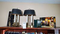 Top shelf with two black and brass lamps, wooden abacus, green bookends, and boxed flameless candle set.