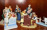 Five Norman Rockwell porcelain figurines displayed on wooden shelf depicting family and domestic life scenes.