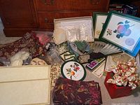 Photo showing a variety of Pimpernel placemats with fruit designs, handcrafted doilies in cloth and crochet, folding wooden and fabric hand fans, playing cards, and decorative tins arranged on a carpet and near wooden furniture.