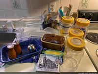 Overview of kitchen items including Pyrex Fridgeware jars, salt and pepper mills, enamelware pan, ceramic dish and trivet, utensils in a container, and kitchen timer.