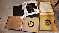 Photo showing multiple vintage 78 RPM records, some loose in paper sleeves and others in album folders with handwritten track listings
