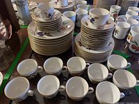 Overall view: two stacks of plates, two stacks of saucers with teacups, row of loose teacups and mugs in back