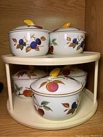 Set of four Royal Worcester Evesham serving bowls with lids arranged on a two-tiered shelf, showcasing fruit pattern and yellow fruit-shaped lid knobs.