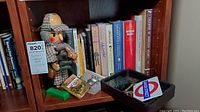 Wide shot of bookshelf containing Sherlock Holmes nutcracker, books including various detective novels, trivia cards, and collectibles arranged on wooden shelves.