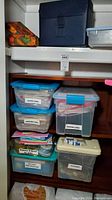 Shelf with multiple labeled clear plastic bins containing stationery, cards, ribbons, paper, and gift wrapping supplies