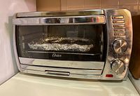 Front view of Oster toaster oven with closed door and control knobs visible.