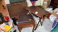 Shows four TV tables with wood grain finish stacked and a wooden footstool with cushioned top in foreground