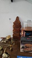 Photo of a carved wooden mail and key holder with butterfly cutouts, brass figurines including an insect and a dog, wooden cake dome with clear cover, and the expandable trivet box visible on a wooden surface.