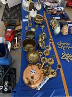 Overview of brass decorations and glass bowl arranged on blue tablecloth showing various brass items including tea pot, bowls, candle holders, horse figurine, and glass bowl.