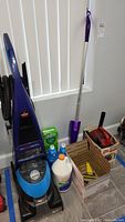 Full front view of the Bissell carpet extractor and surrounding cleaning supplies including Swiffer Jet mop and solution bottles.