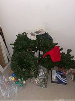 Photo showing artificial Christmas wreaths and garland with bead decorations, red Santa hat, coiled string lights, and other small items on the floor.