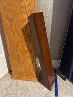 Wood tall CD cabinet with visible oak grain finish and base trim, standing against grey wall and carpet