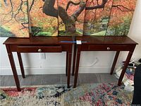 Pair of matching cherry wood color end tables with single drawers and metal knob pulls, shown front facing with one drawer open.