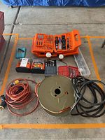 Wide view of the three extension cords, two Black & Decker orange tool cases filled with drill bits and related tools, several smaller bit sets and containers arranged on concrete floor.