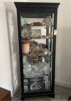 Front view of the tall black wood display cabinet filled with various decorative items to show scale and color.