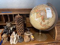 Photo showing the entire lot on a wooden roll-top desk including a 12 inch diameter globe, large pinecone, ceramic wood-styled bear, hand-carved duck, several small bear figurines, and a broken stalactite piece.