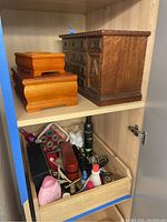 Shelf with two wood jewelry boxes stacked and a drawer containing beauty products and hair styling tools including spray bottles, mousse, nail polish remover, cotton pads, and cords.