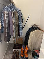 Wide view of closet rod with men's shirts, ties, jackets, boots, and shoe care products on floor