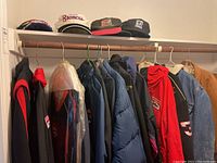 Various men's jackets including windbreakers and coats, plus sports and NASCAR baseball caps displayed on hangers and shelf