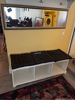 Wall mirror above white foyer bench with three black cushion pads