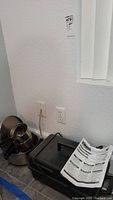 Photo of cooking pots stacked and a black case with instruction manual on top, placed by a wall outlet