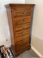 Full view of the tall seven drawer dresser with brass handles and carved crown molding trim.