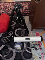 Full overview of telescope tube, adjustable wooden tripod and accessories on floor.