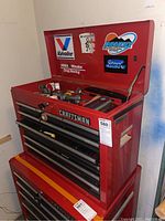 Full view of red Craftsman toolbox with lid open showing automotive stickers on inner lid and multiple metal drawers closed