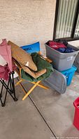 Two plastic totes filled with assorted jackets and sweatshirts, two folding chairs on a concrete floor outside a building.