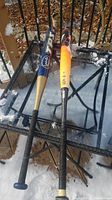 Two composite slow pitch softball bats resting on a snow-dusted glass table; Louisville Slugger TPS bat with blue and gold colors, Easton Wagner bat with yellow and orange colors