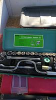 Top-down view showing all 25 pieces of the socket wrench set including multiple sockets, ratchet handle, extensions and spinner handle in green case.