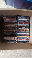 Photo showing a packed box with neatly stacked DVD cases, showing spines of multiple titles revealing genres including action, adventure, and comedy.