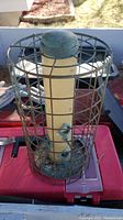 Metal bird feeder 14 inches high with beige seed tube inside a protective metal cage showing some weathering.