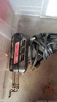 Heat tool with metal heating elements and attached power cord inside plastic bin