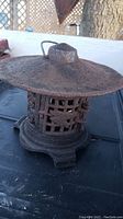 Rusty cast iron tea light holder lantern with a wide flat top and lattice sides, seen from a side angle.