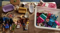 Overview of dolls, puppy figurine and dollhouse furniture spread out including couches, bathtubs and other items.