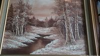 Full view of framed landscape painting showing river, trees, and sky in muted brown and white tones.