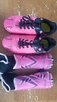 Top view of pink size 2 female soccer cleats and matching shin guards on wooden surface