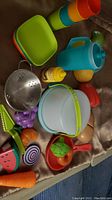 Full assortment of kids Tupperware dishes and play food including plates, cups, pitcher, colander, and many plastic fruits and vegetables.