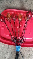 Six metal yard torches with decorative stained glass flower tops in red and amber colors. Shown taped together at base.